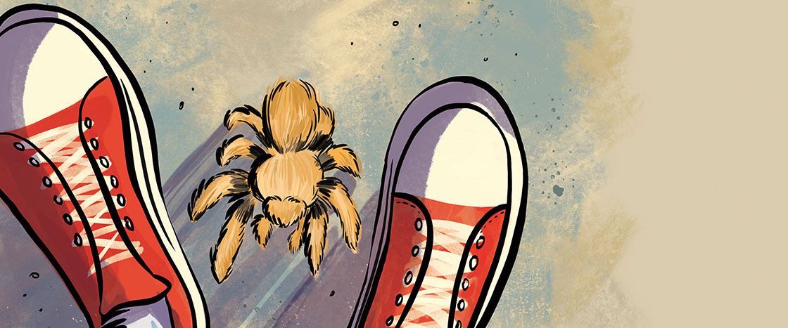 A tarantula sits on the ground between a pair of red sneakers viewed from above
